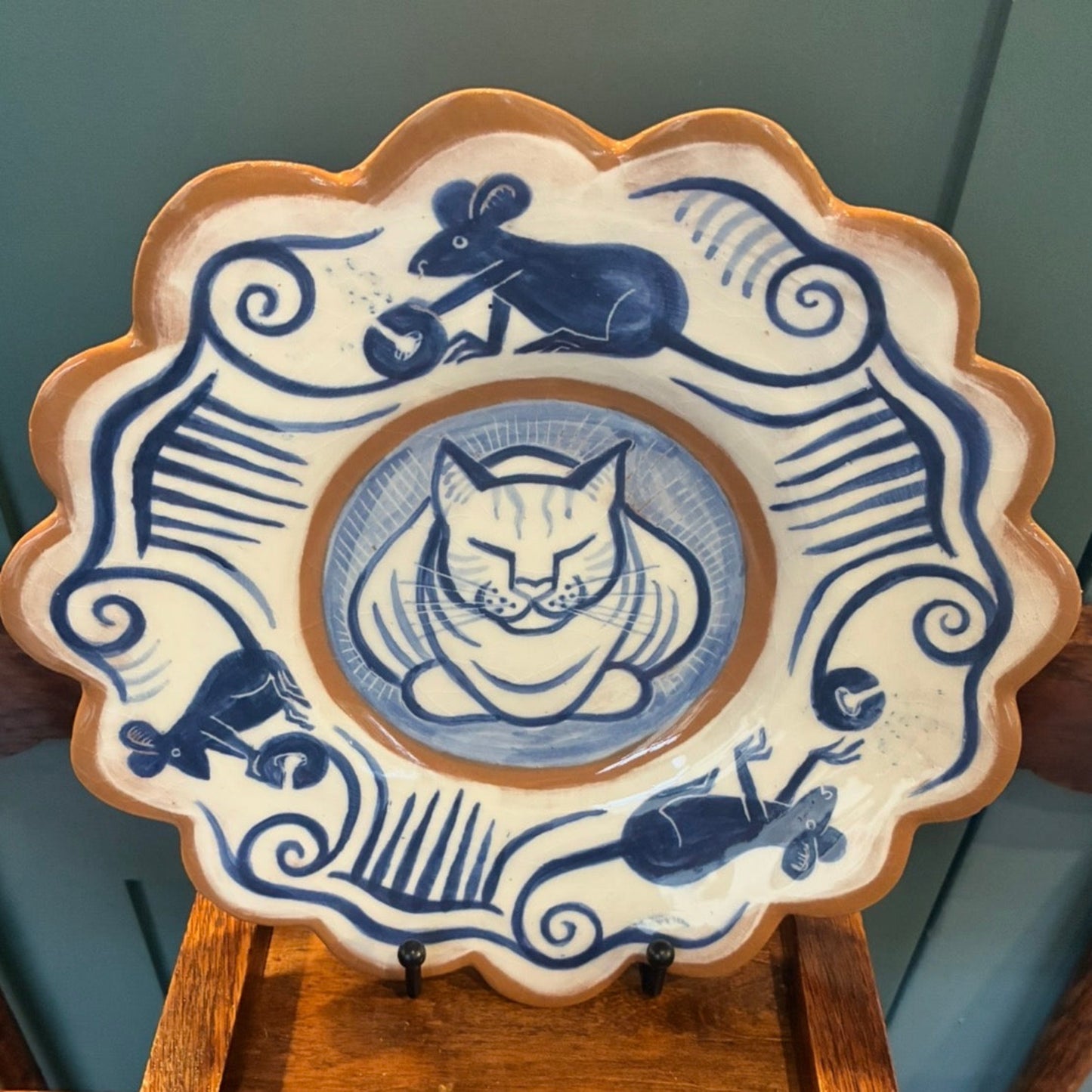 Ceramic plate with blue and white cat design on a wooden stand against a gray background