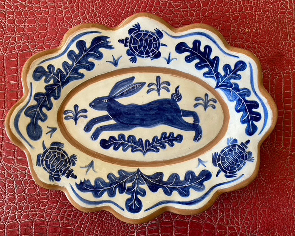 Handmade ceramic plate with a blue hare design surrounded by floral patterns on a white background, with a scalloped edge.