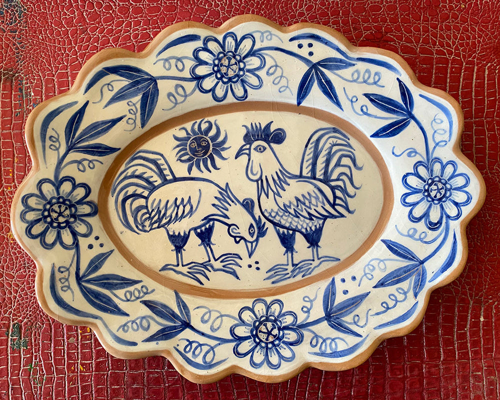 A large blue and white ceramic platter with floral and rooster patterns on a scalloped edge.