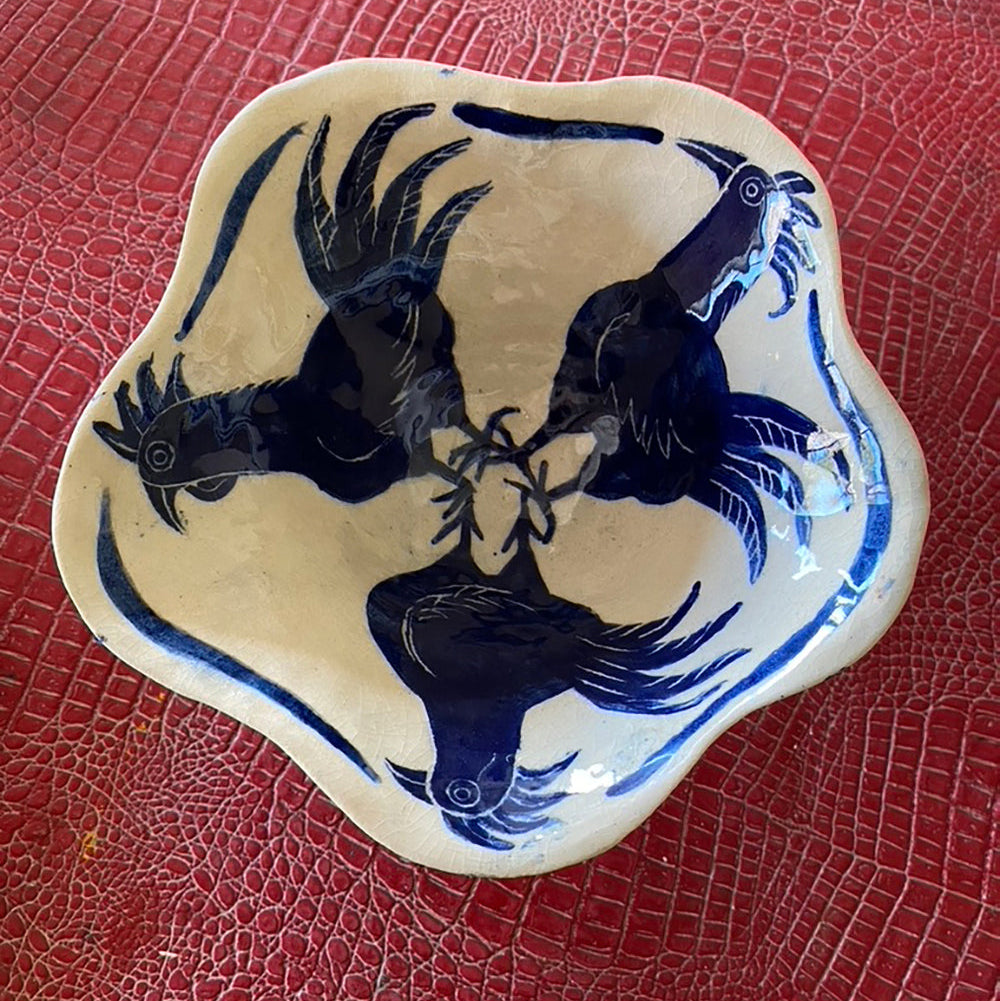 Handmade ceramic bowl with a floral pattern, predominantly blue and white colors, displayed on a red textured surface.