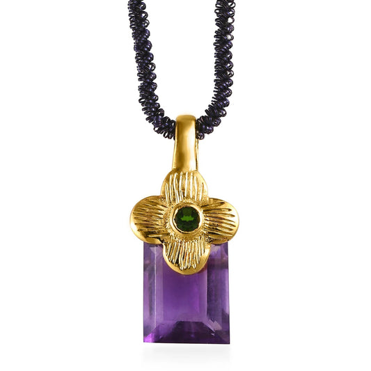 Gold pendant with green gemstone and purple rectangular stone on a black beaded chain against a white background
