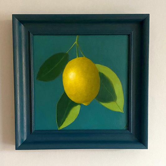 Framed artwork of a lemon with green leaves on a teal background